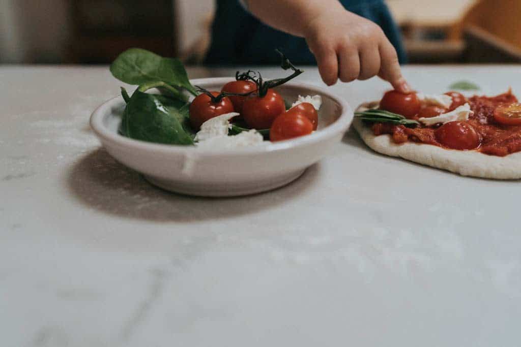 Child putting tomatoes on a pizza