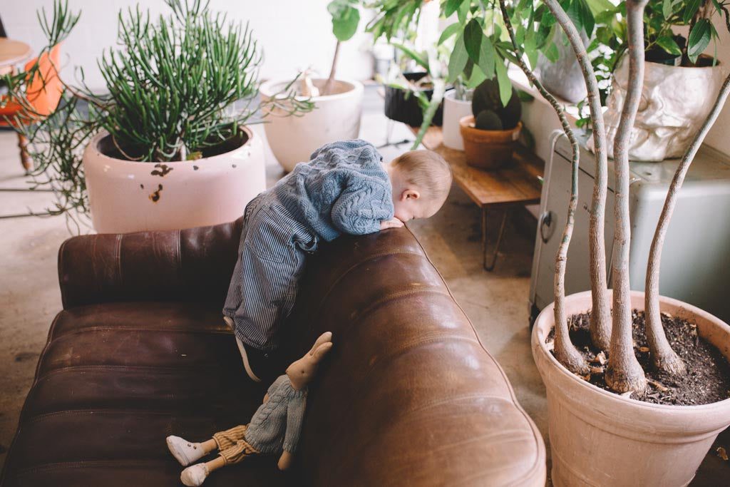 A baby standing on the couch watching its surroundings