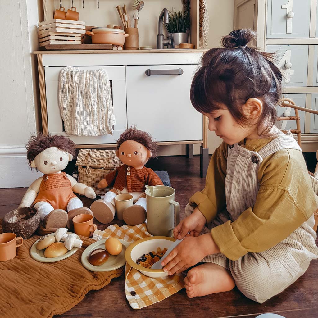 A boy playing with pretend food, dolls and a kitchen