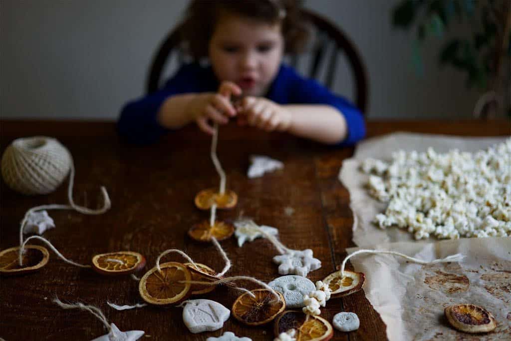 A child threading orange slices and popcorn