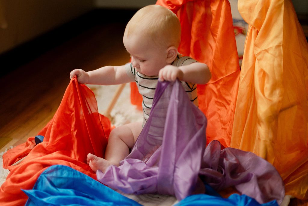 A baby enjoying heuristic play with a playsilk