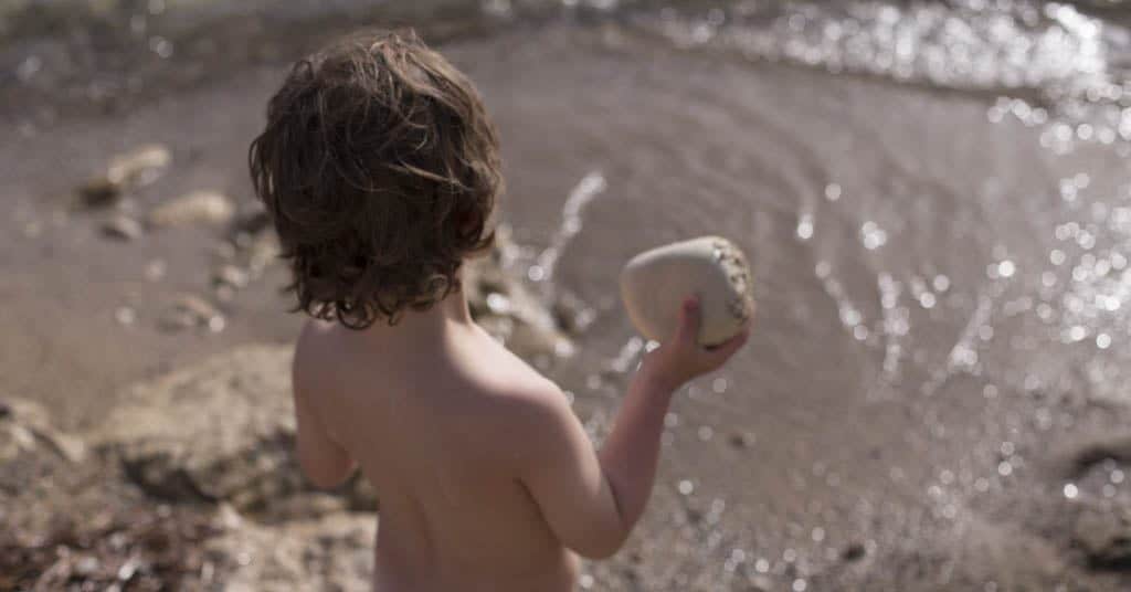 A boy throwing a rock into the sea