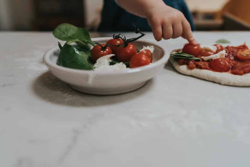 A child pressing a tomato onto a pizza