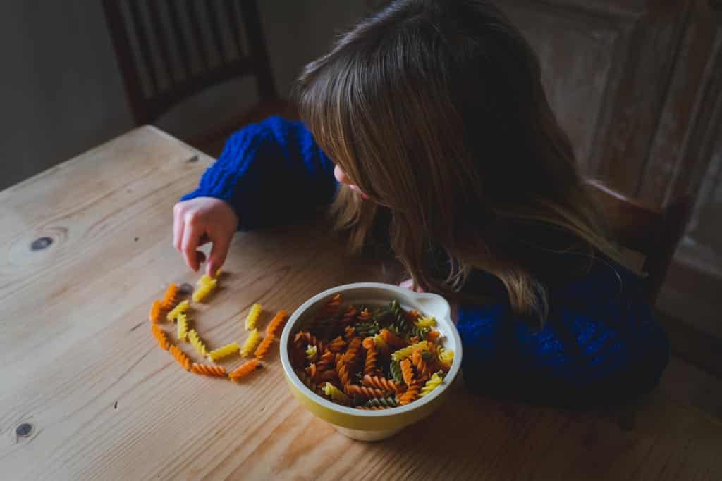 A child positioning pasta pieces in a row