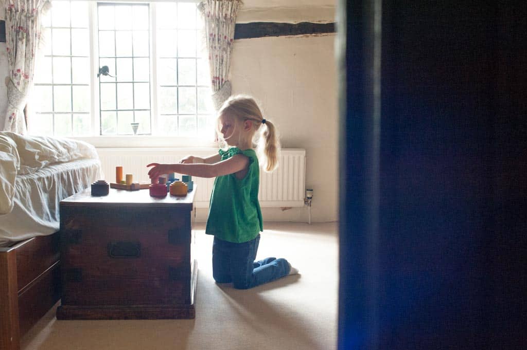 Young child playing independently with colorful wooden blocks on a table in a sunlit, cozy room.