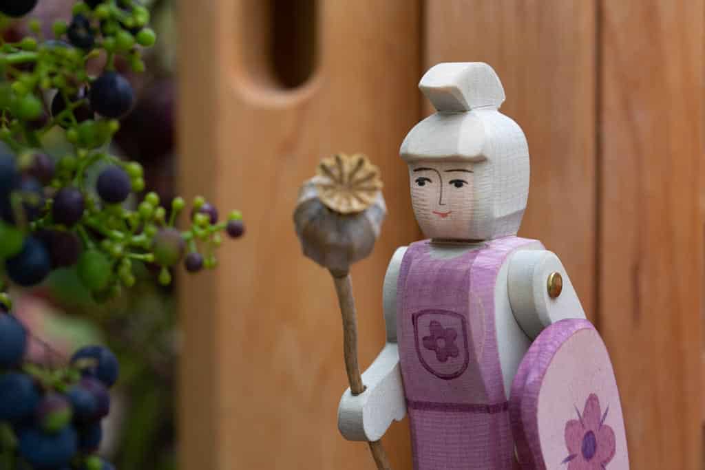 Wooden doll house figure dressed as a knight with a flower staff, encouraging imaginative play and problem-solving skills in preschoolers.