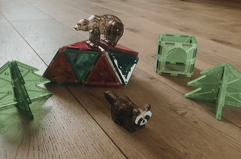 Magnetic building blocks arranged as a forest scene with green trees, a cube, a raccoon figure lying on the floor.